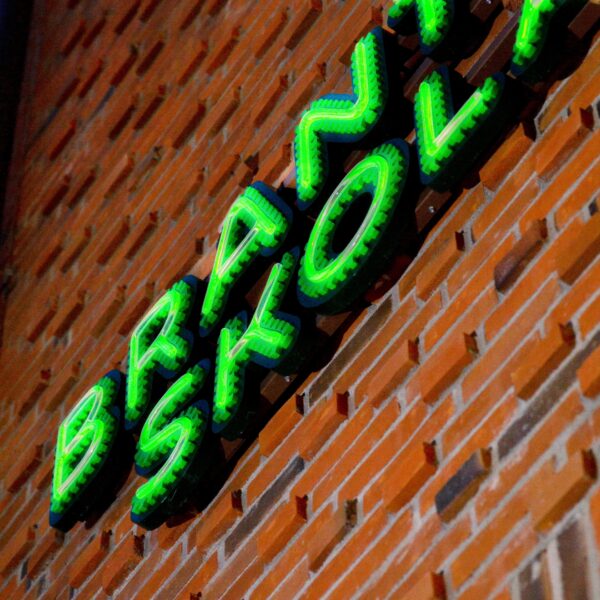 Fasadskylt med individuella profilbokstäver i grön lackerad aluminium, centrerade konturfrästa toppbokstäver och grön LED-neon i rundglansig akryl - Bild 8