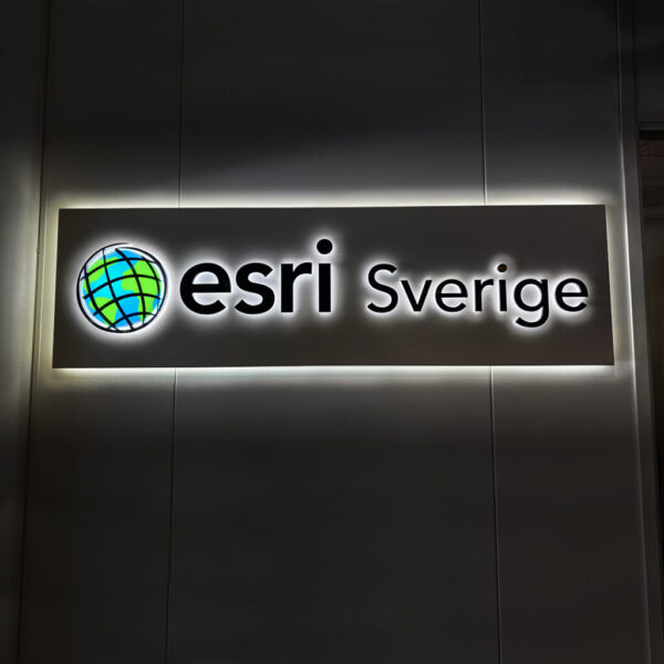 Receptionsskylt med vit bakgrundsplatta och LED-bakbelysning, svarta profilbokstäver i lackerat rostfritt stål samt dubbelbelyst logotyp med digitaltryckt dekor och akryltopp