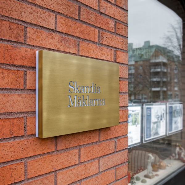 Fasadskylt i borstad guldtitanlegerat rostfritt stål med dekaperad LED-belyst logotyp och delvis belyst kant i opalvit akryl - Bild 5