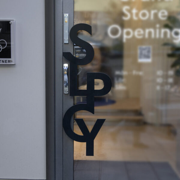 Dörrskylt i form av handtag i svartlackerat rostfritt stål – metallformad logotyp som funktionellt dörrhandtag för butikens entré