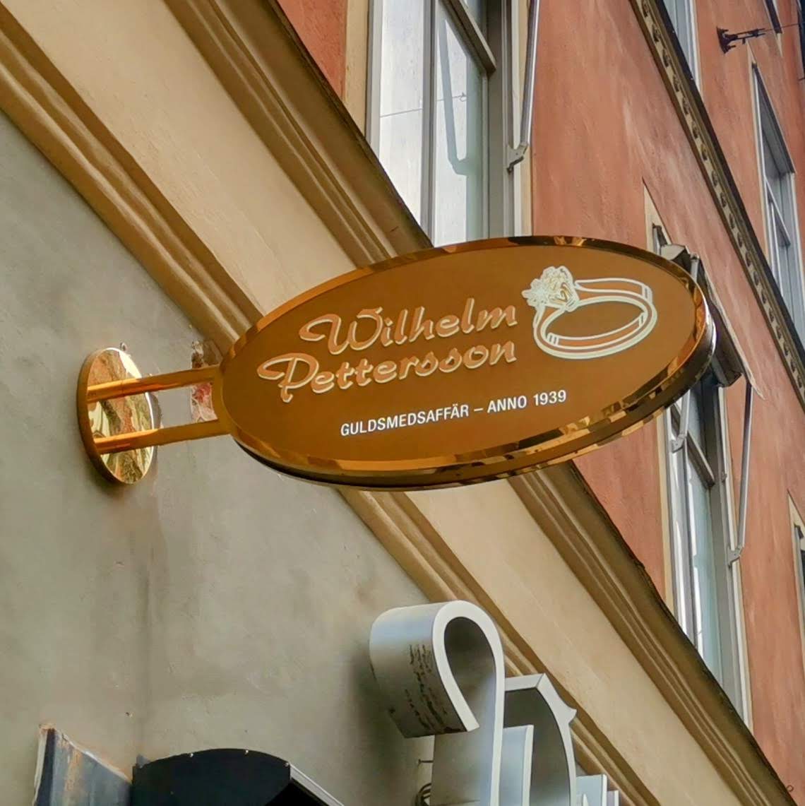 Dubbelsidig oval flaggskylt med borstad guldtitanlegerad bakgrund, sido-LED-belysta profilbokstäver och blankpolerad ram, sarg och rundrörsinfästning