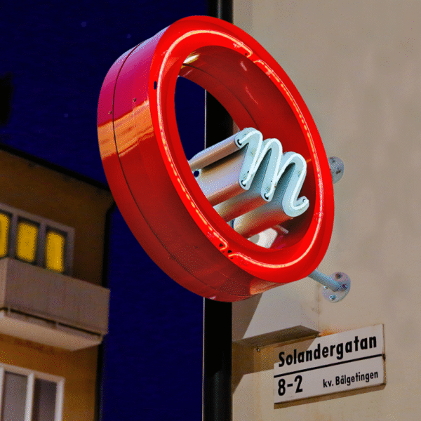 Flaggskylt i rund form med genombruten glasneonlogotyp och upphöjd kant med integrerad glasneonbelysning