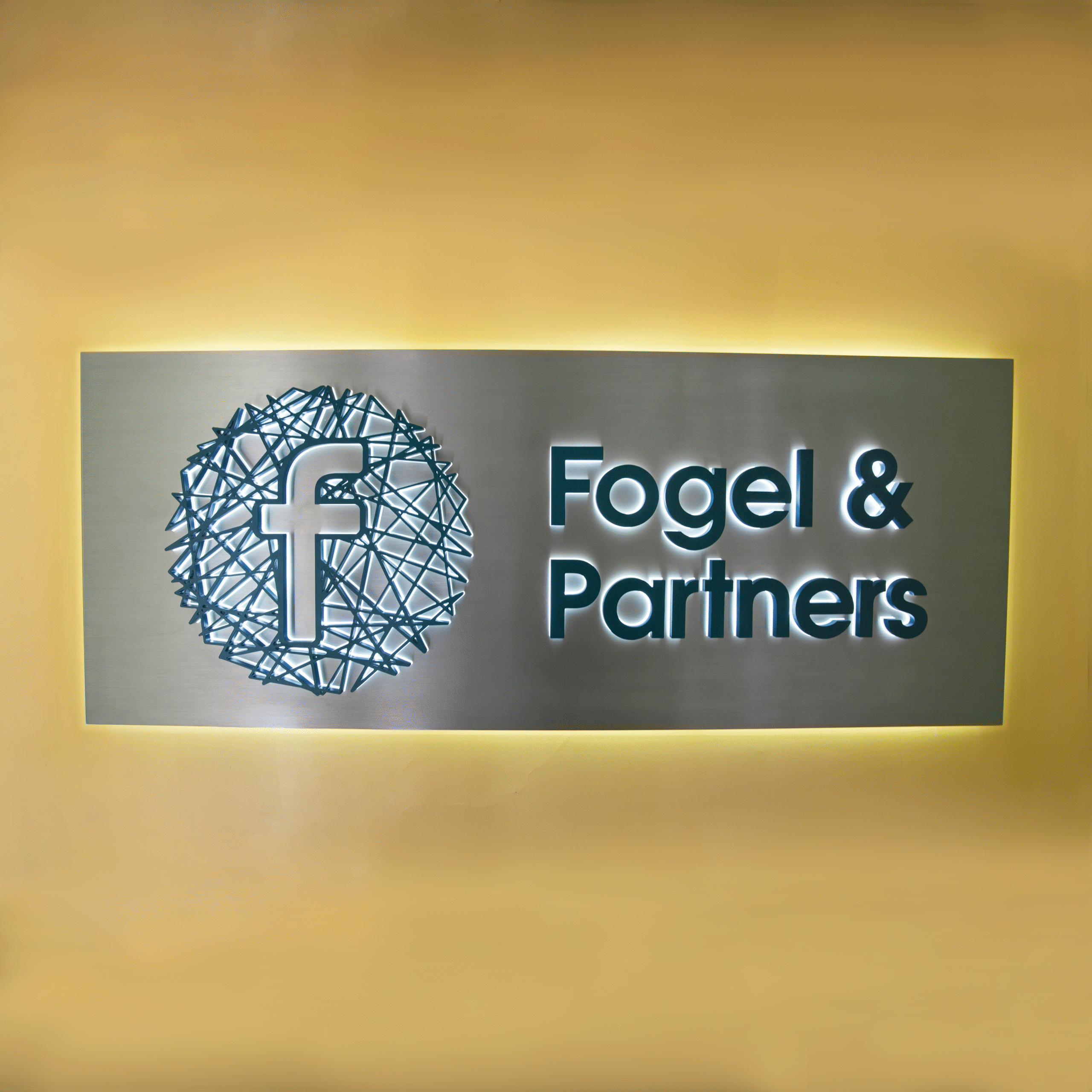 Fogel & partner Receptionsskylt i borstat rostfritt stål med bakbelysning, laserskuren skulpturell logotyp och LED-belysta profilbokstäver med opalvit och blå delkant