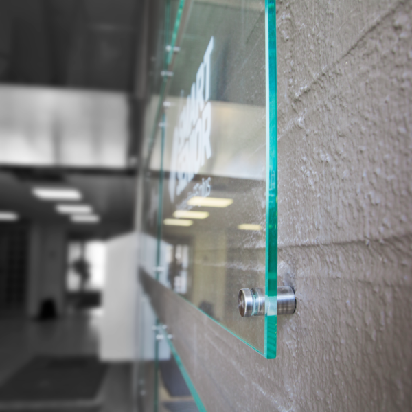 Receptionsskylt i optiwhite härdat glas med vinyldekor monterad med rostfria distansbeslag – del av en vägginstallation med flera logotyper - Bild 4