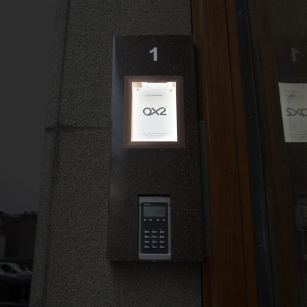 Fastighetsskylt som infoskåp i Corian med glasdörr och borstade kopparkantlister – porttelefoninkapsling med appstyrd belysning och lås