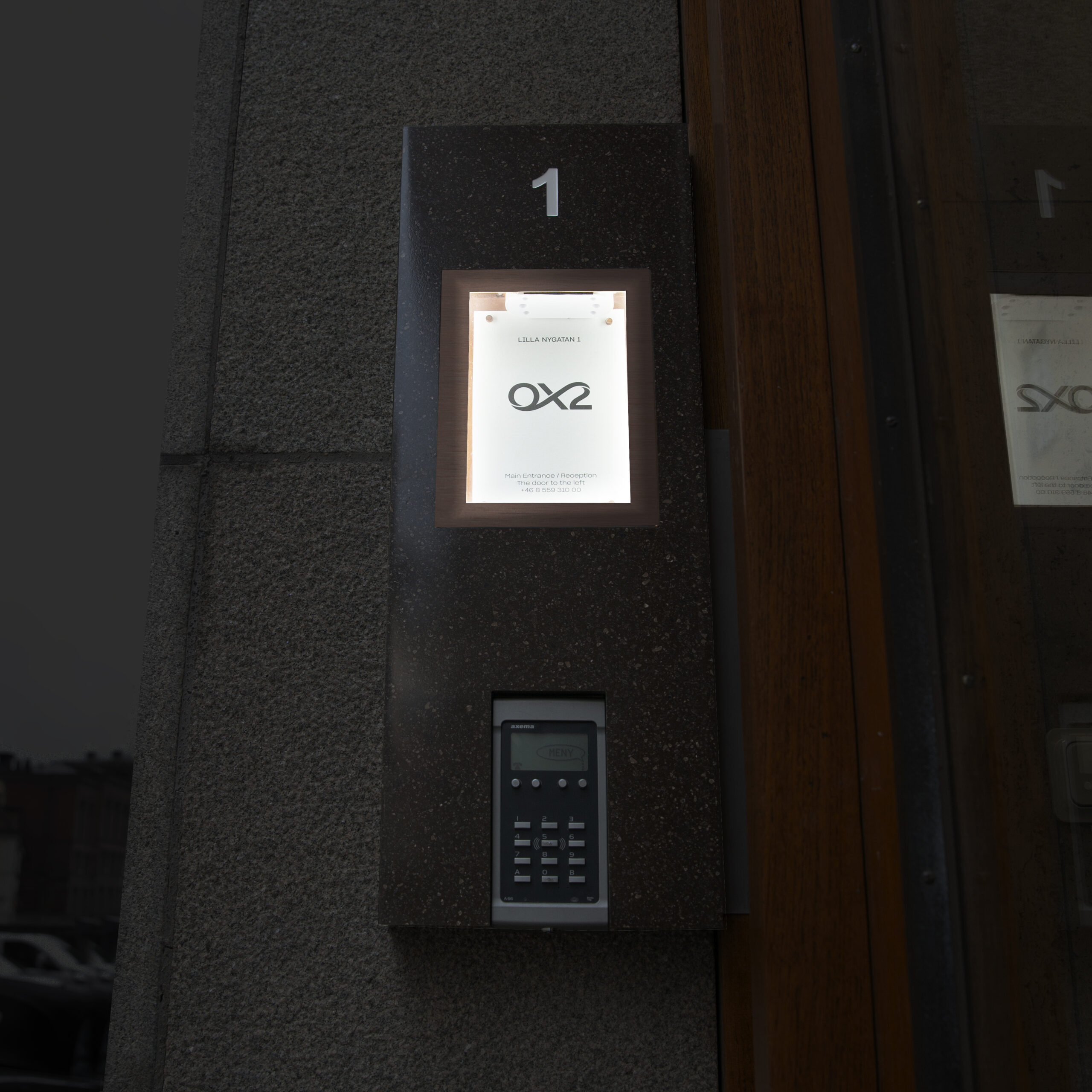 Fastighetsskylt som infoskåp i Corian med glasdörr och borstade kopparkantlister – porttelefoninkapsling med appstyrd belysning och lås