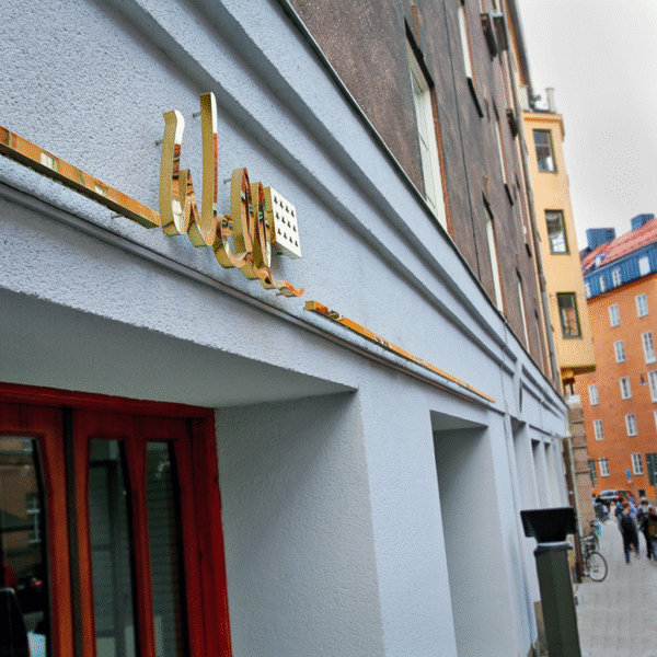 Fasadskylt i blank guldtitanlegerat rostfritt stål med bakbelysta profilbokstäver och ljusramper – distansmonterad för halo-effekt
