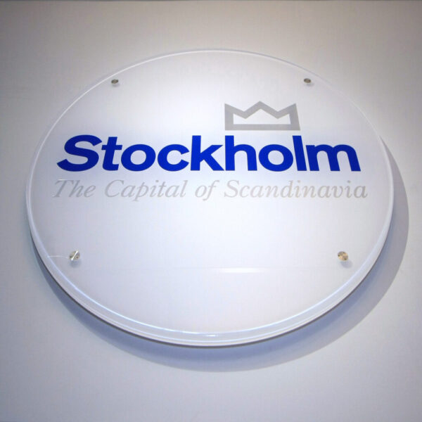 Receptionsskylt i rund transparent akryl med baksidedekor och distansmontering från vägg med distansbeslag