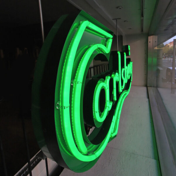 Fasadskylt i grön lackerad aluminium med förhöjd sarg, skärmningskant och grön LED-neon – monterad på insidan av fasadfönster - Bild 4