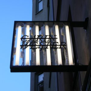 Flaggskylt Carin Wester med synliga lysrör och svart akryl